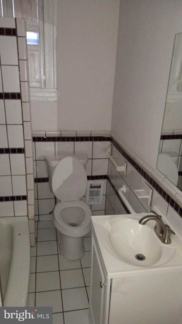 bathroom featuring tile walls, vanity, tile patterned floors, a tub, and toilet