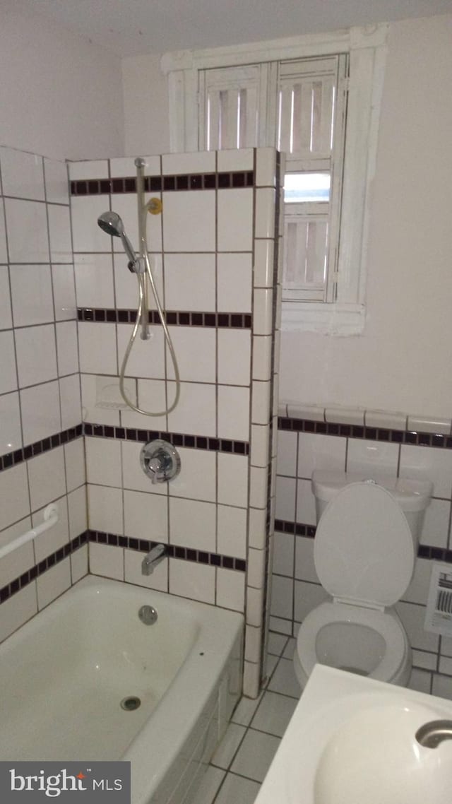 bathroom with a washtub, toilet, and tile walls