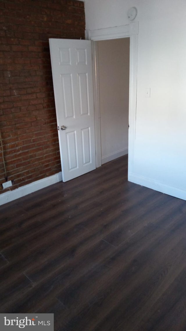 unfurnished room featuring brick wall and dark wood-type flooring