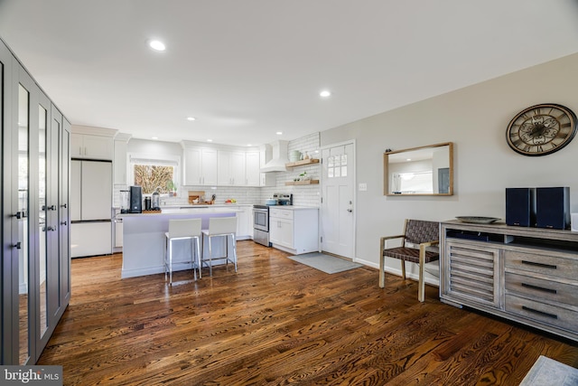 kitchen featuring a kitchen breakfast bar, stainless steel range with electric stovetop, white refrigerator, a kitchen island, and white cabinetry