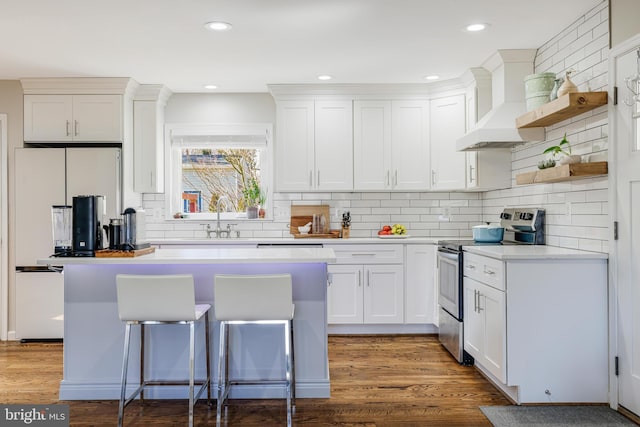 kitchen featuring hardwood / wood-style floors, a breakfast bar, stainless steel range with electric stovetop, white cabinetry, and premium range hood