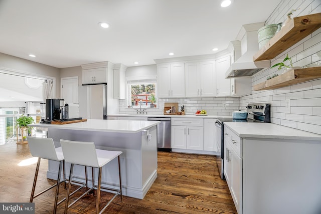 kitchen featuring white cabinetry, stainless steel appliances, a breakfast bar, a center island, and premium range hood