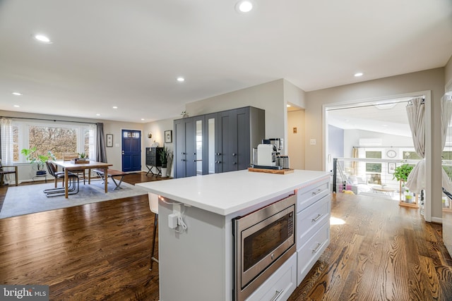 kitchen with white cabinetry, a center island, a breakfast bar, hardwood / wood-style floors, and stainless steel microwave