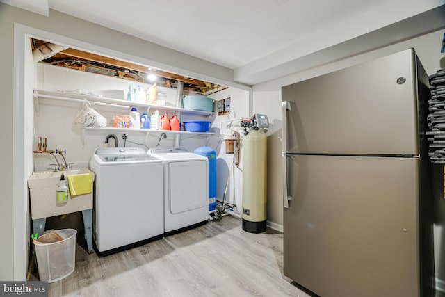 clothes washing area with light hardwood / wood-style floors, washing machine and dryer, and sink