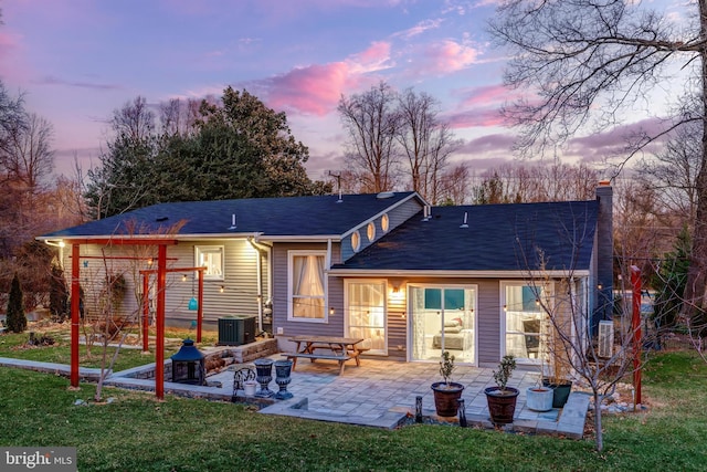 back house at dusk featuring central air condition unit, a patio area, and a yard