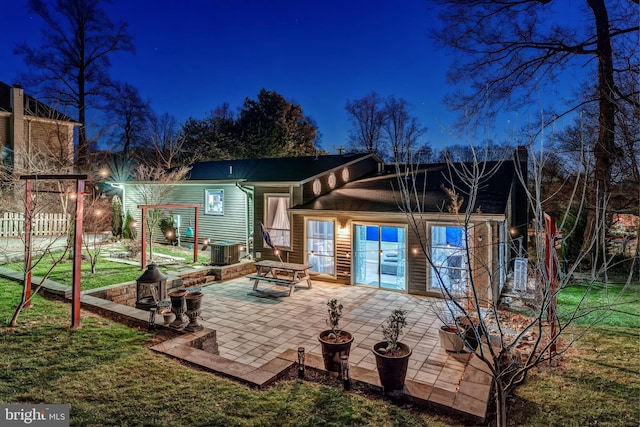 back house at night featuring a patio area, central AC unit, a lawn, and a fire pit