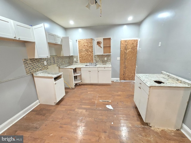 kitchen with tasteful backsplash, light stone counters, white cabinets, and light wood-type flooring