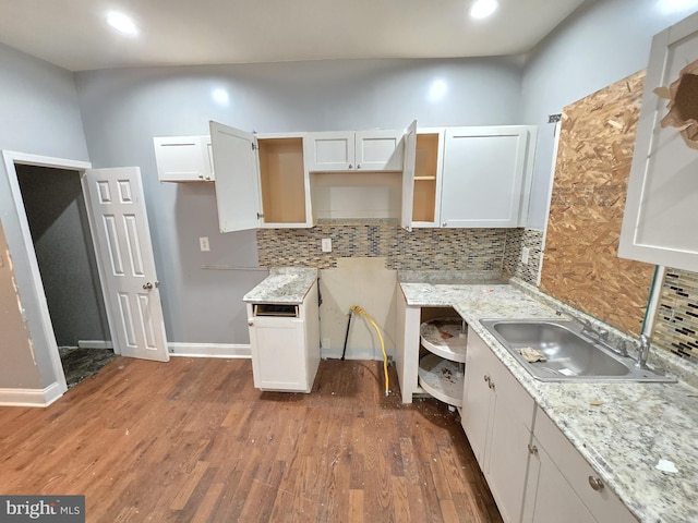 kitchen with sink, white cabinets, decorative backsplash, light stone counters, and dark wood-type flooring