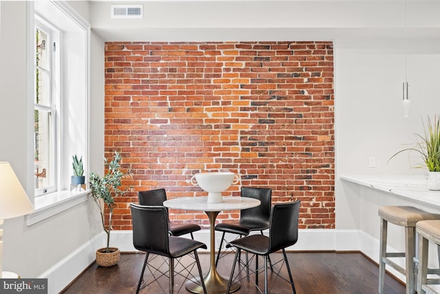 dining area with dark hardwood / wood-style floors and brick wall