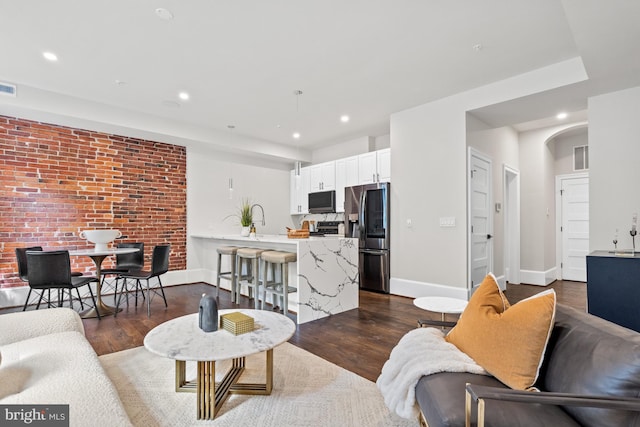 living room featuring sink, dark wood-type flooring, and brick wall