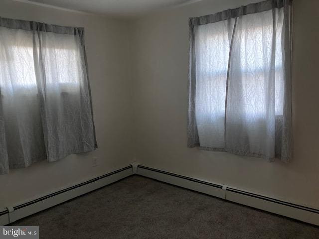 empty room featuring dark carpet and a baseboard heating unit