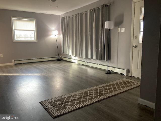 spare room featuring ceiling fan, dark wood-type flooring, and a baseboard heating unit