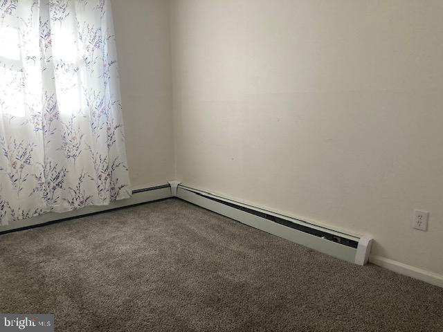 carpeted spare room featuring a baseboard heating unit