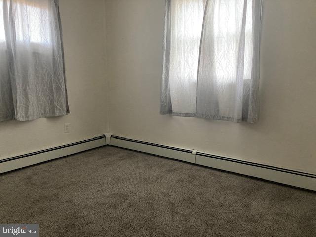 carpeted empty room with a baseboard heating unit