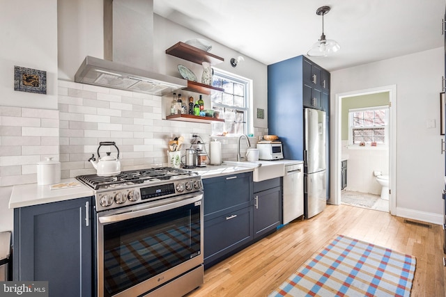 kitchen with light countertops, appliances with stainless steel finishes, light wood-style floors, plenty of natural light, and wall chimney exhaust hood