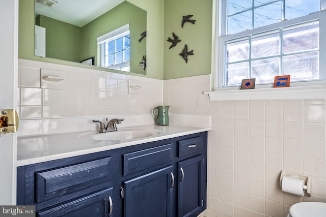 bathroom featuring toilet, visible vents, vanity, tile walls, and wainscoting