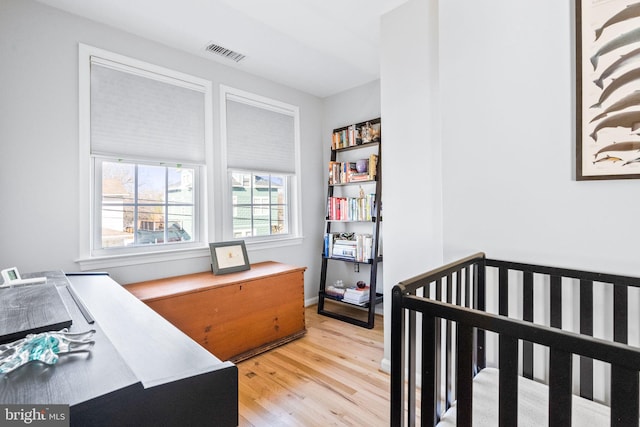 bedroom with light wood-type flooring, a nursery area, and visible vents