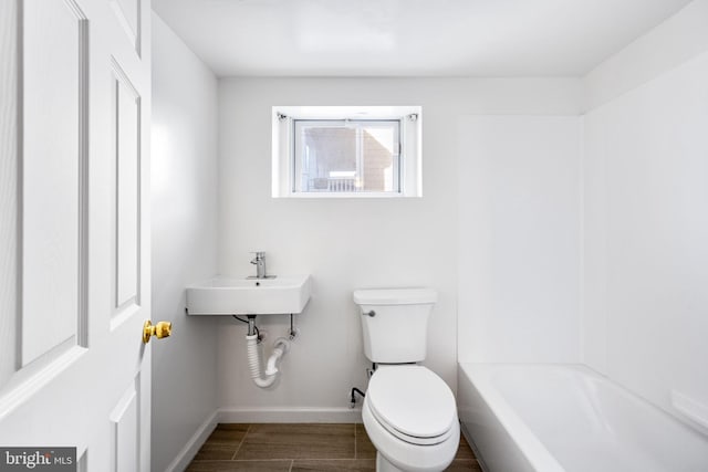 bathroom with toilet, a sink, wood finished floors, a tub, and baseboards