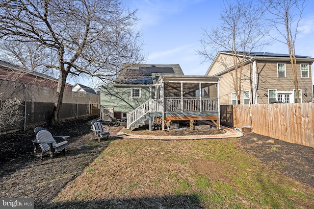 back of property with a sunroom, a fenced backyard, a yard, and solar panels