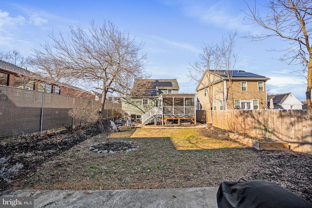 back of property featuring a sunroom, a fenced backyard, and roof mounted solar panels