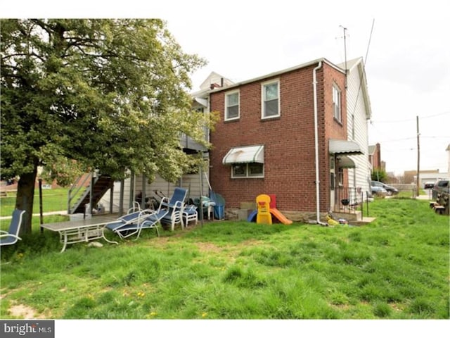 back of house with brick siding and a yard