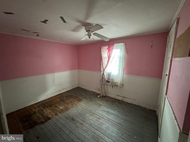 unfurnished room with crown molding, ceiling fan, wood finished floors, and wainscoting