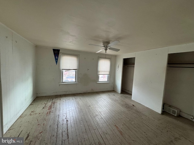 unfurnished bedroom with a ceiling fan, light wood finished floors, and two closets