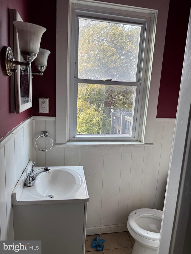 half bathroom featuring wainscoting, vanity, toilet, and tile patterned floors