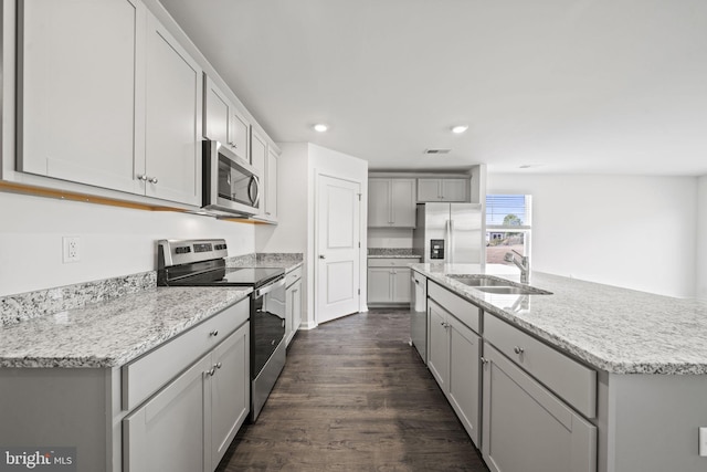 kitchen with sink, gray cabinets, appliances with stainless steel finishes, a kitchen island with sink, and dark hardwood / wood-style flooring