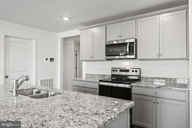 kitchen with light stone counters, appliances with stainless steel finishes, gray cabinets, and sink