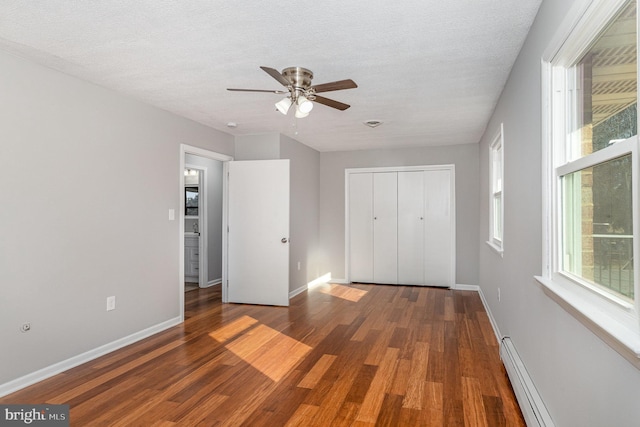 unfurnished bedroom with a baseboard heating unit, dark wood-type flooring, a closet, and a textured ceiling