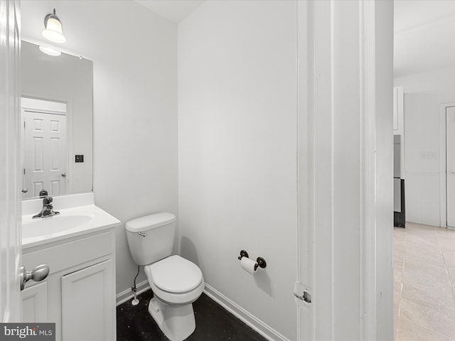 half bath with baseboards, vanity, and toilet