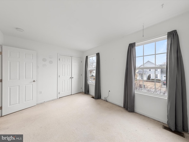 unfurnished bedroom with a closet, visible vents, light carpet, and baseboards