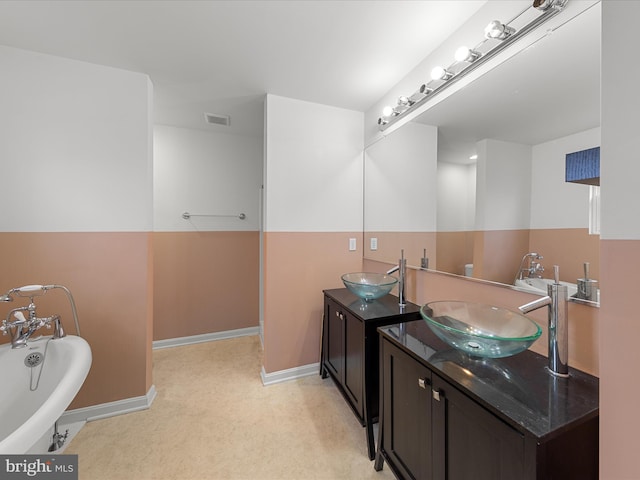 bathroom with a freestanding tub, visible vents, vanity, and baseboards