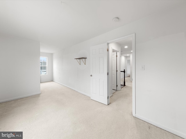 spare room featuring light colored carpet and baseboards