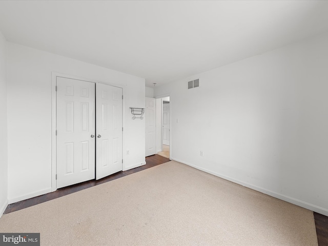 unfurnished bedroom with dark wood-style flooring, a closet, visible vents, and baseboards