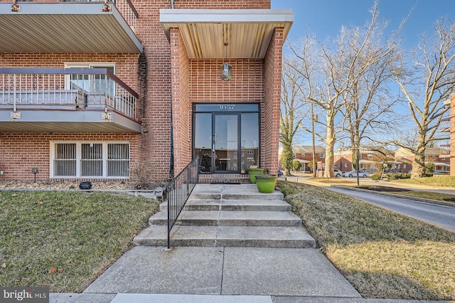 property entrance featuring brick siding, a lawn, and a balcony