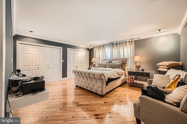 bedroom with light wood-style flooring, multiple closets, and ornamental molding