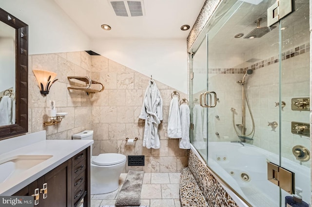 bathroom with visible vents, toilet, vanity, stone tile floors, and tile walls