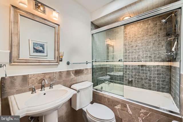 full bath featuring tiled shower / bath combo, toilet, tile walls, and a sink