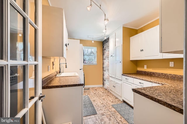 kitchen featuring white cabinetry, dark countertops, crown molding, and a sink