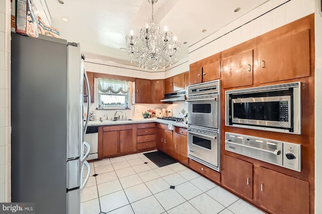 kitchen featuring a sink, under cabinet range hood, appliances with stainless steel finishes, a warming drawer, and a notable chandelier