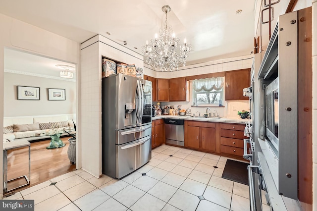 kitchen featuring light countertops, brown cabinets, appliances with stainless steel finishes, a notable chandelier, and a sink