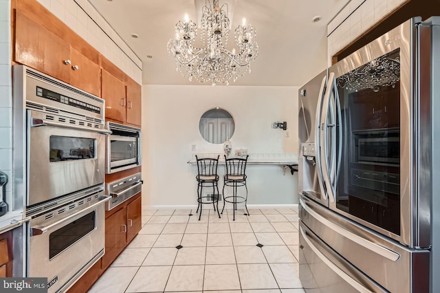 kitchen with a warming drawer, brown cabinets, a notable chandelier, stainless steel appliances, and light tile patterned floors