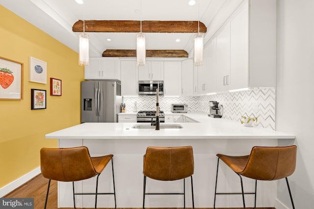 kitchen with a breakfast bar area, stainless steel appliances, pendant lighting, white cabinetry, and kitchen peninsula