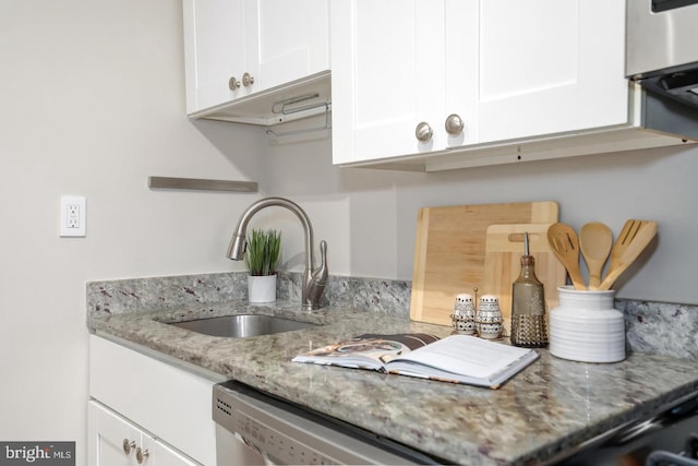 kitchen featuring stainless steel dishwasher, sink, light stone counters, and white cabinets