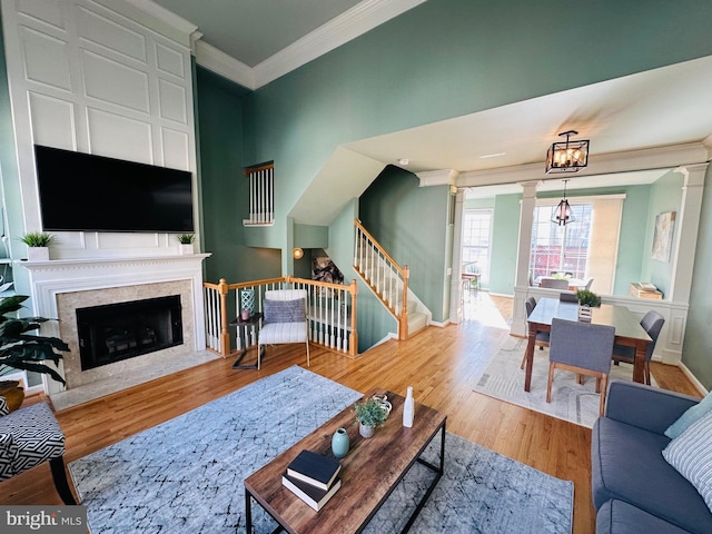 living area featuring a premium fireplace, wood finished floors, ornamental molding, stairway, and decorative columns