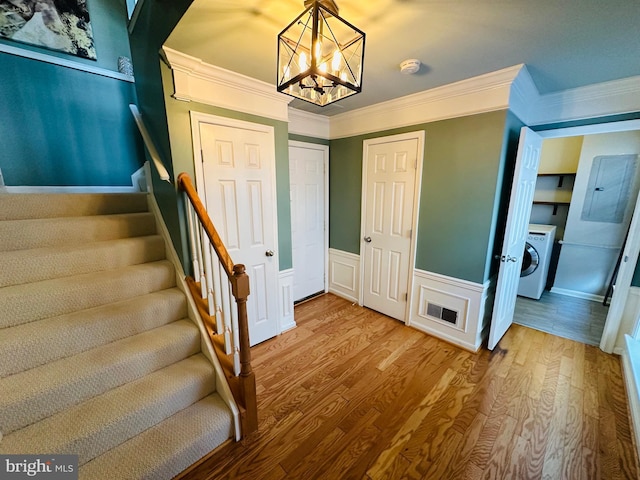 staircase featuring wood finished floors, visible vents, wainscoting, washer / dryer, and crown molding