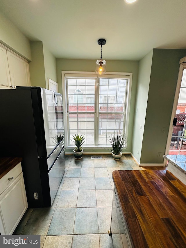 kitchen with decorative light fixtures, light tile patterned floors, freestanding refrigerator, white cabinets, and baseboards