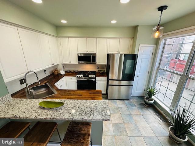 kitchen with white cabinets, a peninsula, a sink, stainless steel appliances, and backsplash